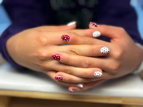 Sa pose : des mains croisées aux ongles à pois rouges et blancs