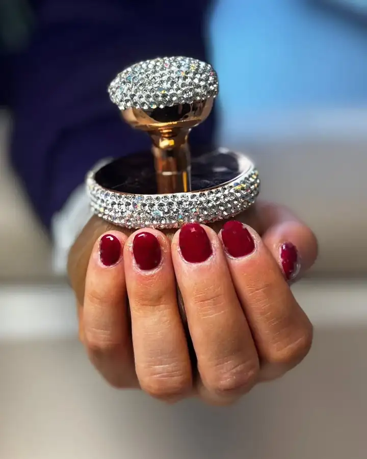 Sa main aux ongles bordeaux autour d'un flacon à strass ; au défilement, les pois blancs se posent un à un